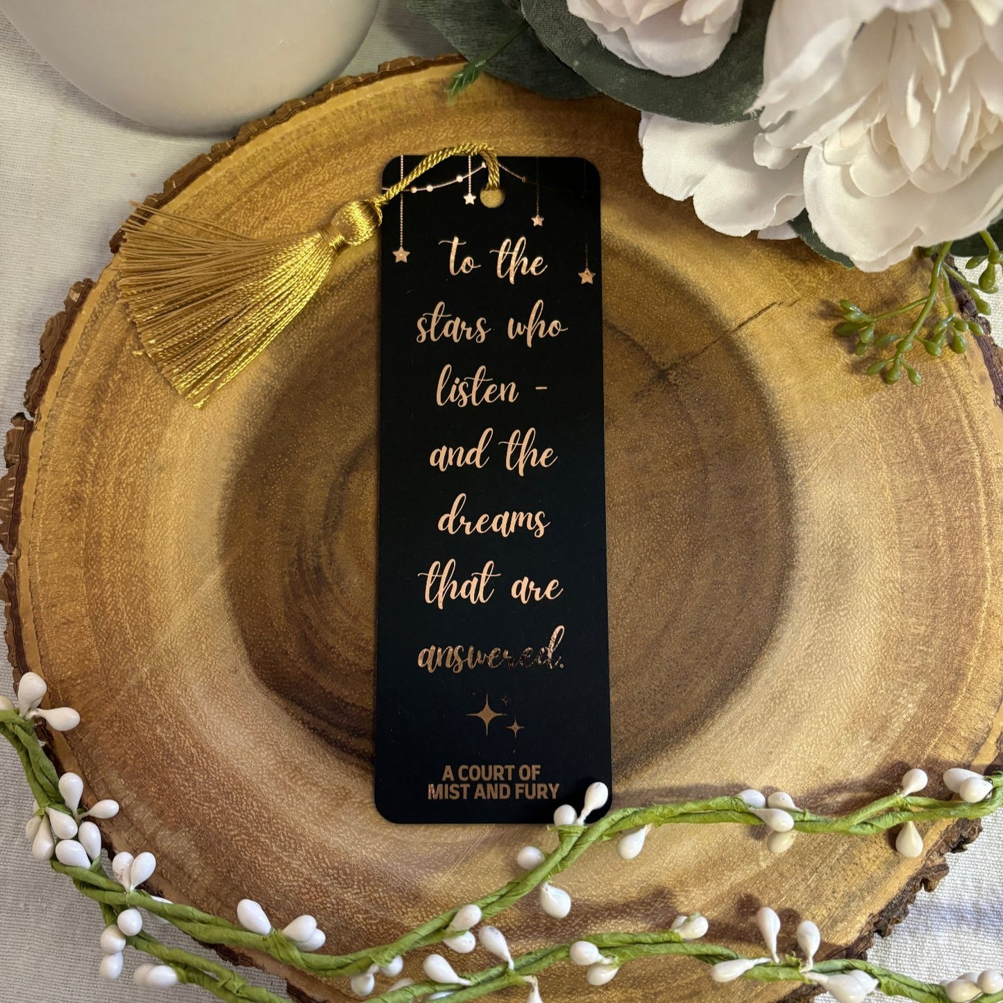 black bookmark with rose gold writing and gold tassel handing from hole at the top. quote reads, "to the stars who listen and the dreams that are answered"