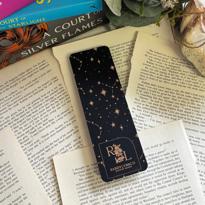 backside of rose gold foil bookmark laid out on loose book pages. constellation pattern with logo